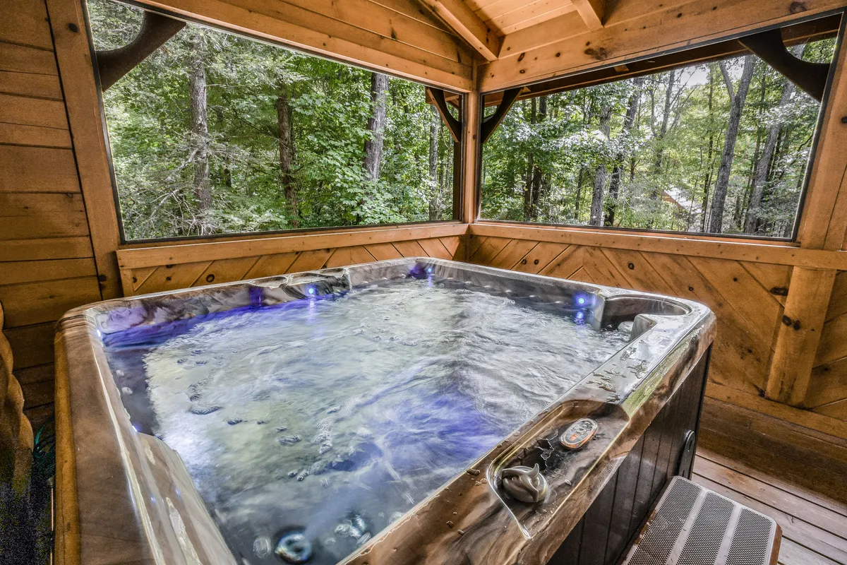 A tranquil hot tub nestled within a wooden structure, open to lush green views. The setup captures the relaxing transition from outdoor adventure to rejuvenation, with the surrounding foliage providing a soothing backdrop.