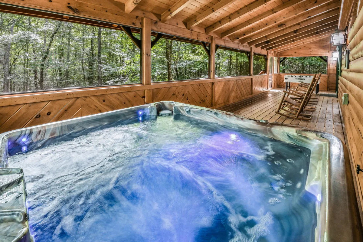 This image features a hot tub set within a wooden structure, surrounded by lush greenery visible through screened openings. The tranquil scene captures the rejuvenating ambiance of soaking in the hot tub while feeling immersed in the forest setting.