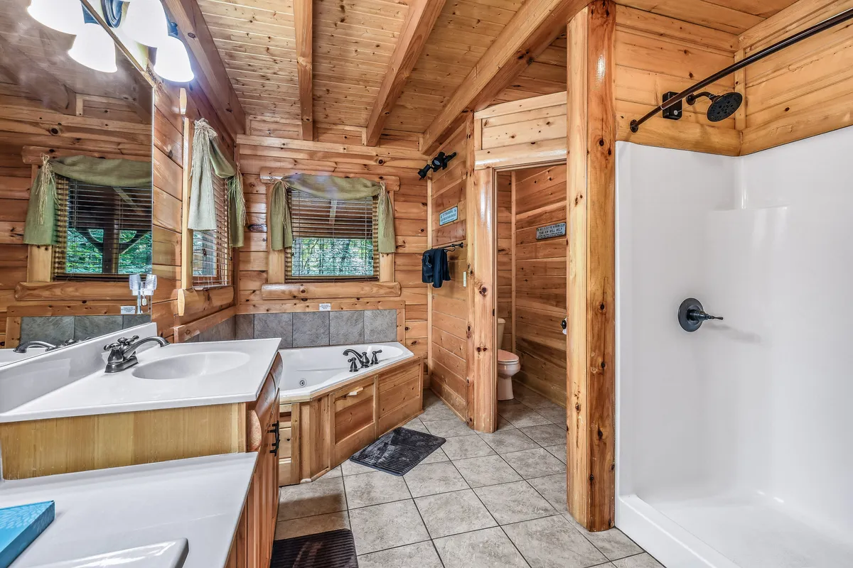 A tranquil master bathroom featuring a jacuzzi tub, double sink vanity, shower stall, and exposed wooden beams. The space is cozy and serene, perfect for unwinding after adventurous days.