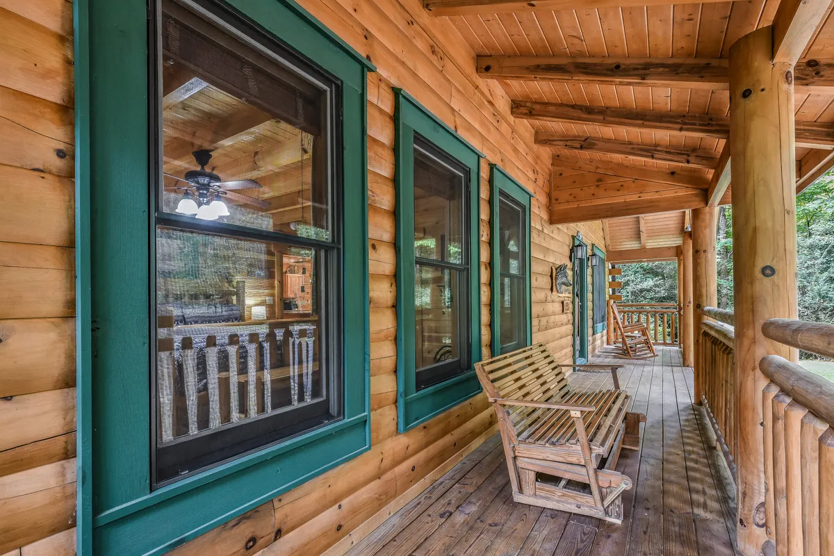 A serene porch scene with a wooden rocking chair facing out toward the natural landscape, framed by large windows and a wooden railing. The atmosphere is tranquil and inviting, ideal for sipping coffee or connecting with loved ones.