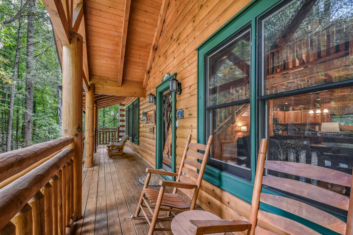 An inviting exterior view of the cabin’s porch, featuring wooden rocking chairs looking out over lush greenery. The log cabin structure is visible, and the peaceful surroundings encourage relaxation, sunrise coffee moments, and evening star-gazing.