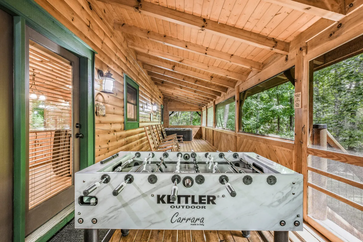 A spacious wooden deck features a foosball table and an outdoor seating area, set against a backdrop of natural greenery. The setup encourages friendly competition and casual conversations in the fresh mountain air.