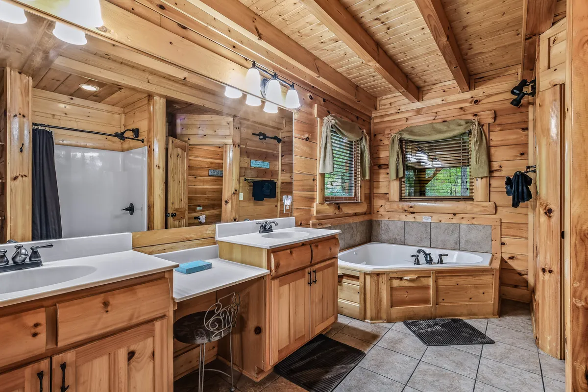 A serene ensuite bathroom with double sinks, a spacious bathtub, large mirrors, and wooden accents. A window provides natural light and a peaceful view, creating a spa-like atmosphere for relaxation after a day outdoors.
